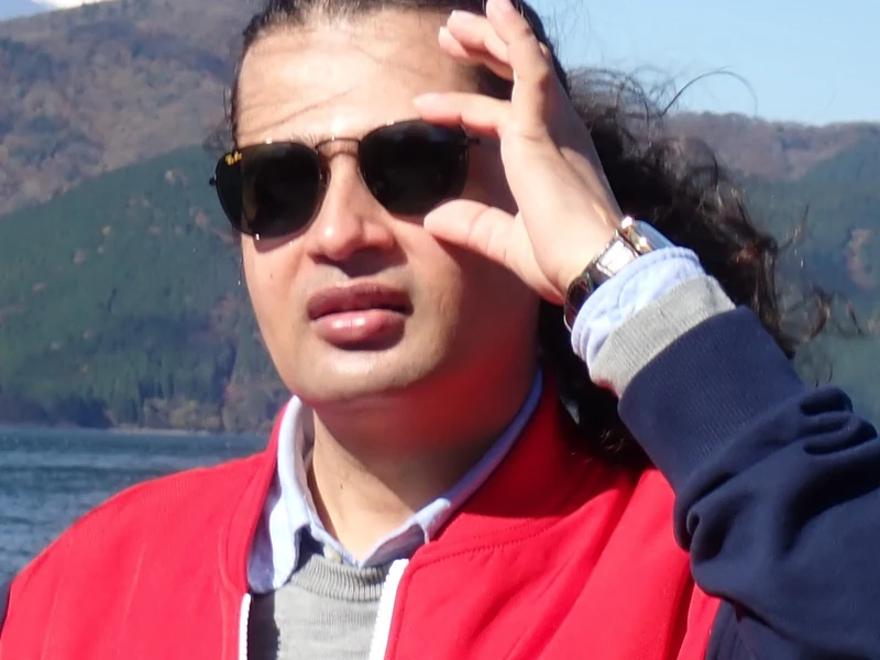 Close portrait of Dr. Ram C. Sharma wearing sunglasses beside a mountain lake.