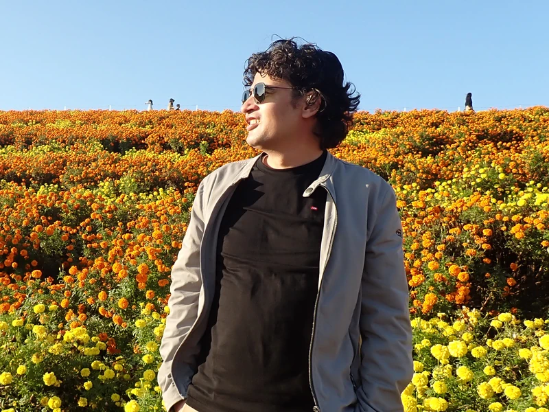 Dr. Ram C. Sharma wearing sunglasses among rows of orange and yellow flowers.
