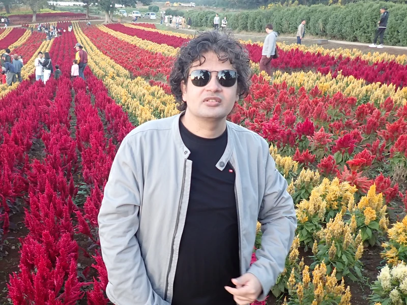 Dr. Ram C. Sharma wearing sunglasses amid vivid seasonal flower beds.