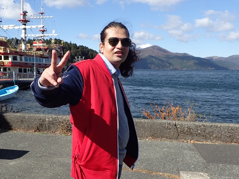 Dr. Ram C. Sharma wearing sunglasses beside a lake and sightseeing boat.