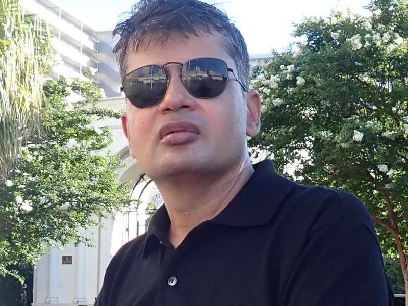 Sunlit outdoor portrait of Dr. Ram C. Sharma wearing sunglasses and a black polo shirt.