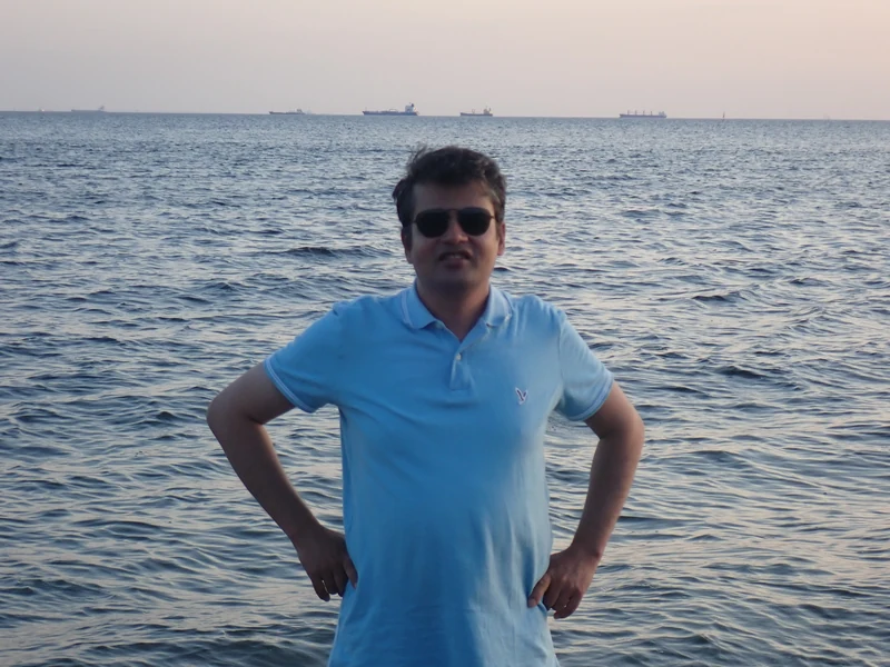 Dr. Ram C. Sharma wearing sunglasses at the waterfront in soft evening light.