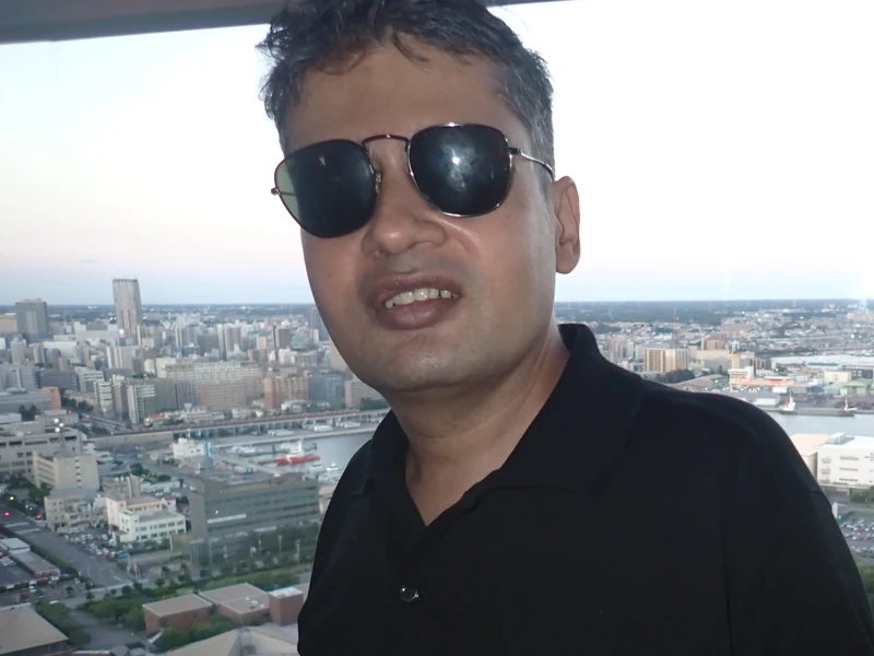 Dr. Ram C. Sharma wearing sunglasses at an observation point overlooking an urban landscape.