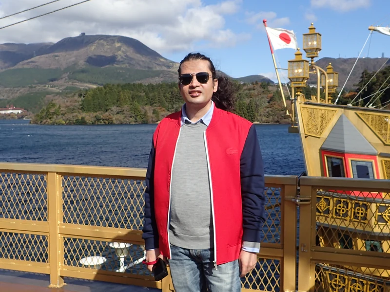 Dr. Ram C. Sharma wearing sunglasses on a sightseeing deck with mountains in the background.