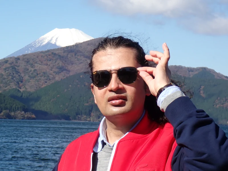 Close portrait of Dr. Ram C. Sharma wearing sunglasses with a lake and mountain backdrop.